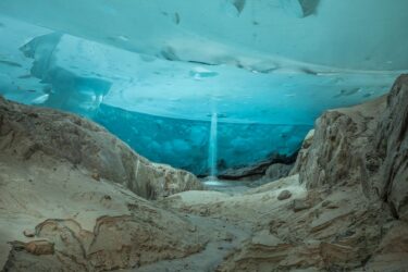 Cascade débouchant d'un petit moulin dans une grande salle dont la hauteur pouvait approcher les 8 mètres. Ce plafond parfaitement plat est-il le témoin d'un ancien régime noyé ? Glacier d'Aletsch. Lumière exclusivement naturelle filtrant à travers la glace.